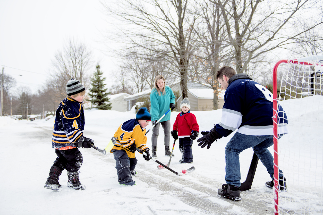 Happy funny kids playing hockey with father and mother on street in the ...